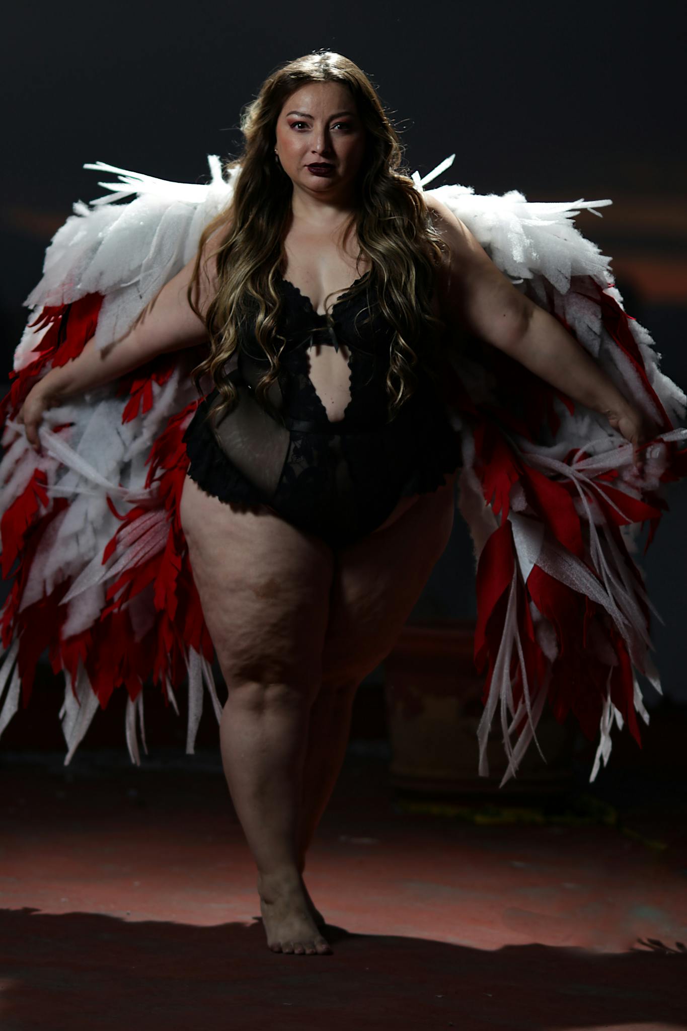 Confident plus-size woman in black lingerie and angel wings embodies empowerment.